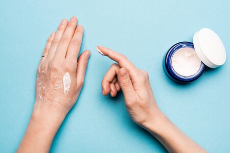 cropped view of woman applying hand cream on dehydrated, exfoliated skin on blueの写真素材