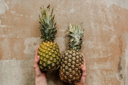 cropped view of woman holding ripe pineapples on weathered surfaceの写真素材