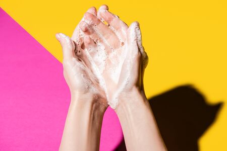 cropped view of female hands in soap foam on pink and yellowの写真素材