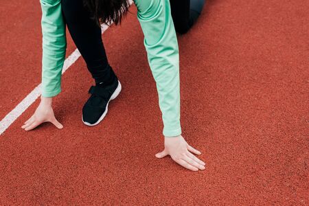 Cropped view of sportswoman standing in starting position on running path