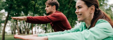 Selective focus of smiling woman training near boyfriend in park, panoramic shotの写真素材