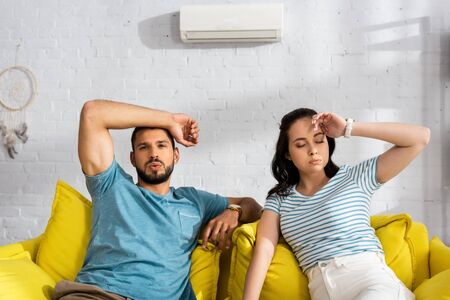 Tired couple suffering from heat while sitting on sofa at homeの写真素材