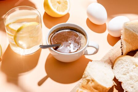 coffee, eggs, baguette and glass of water for breakfast on beige tableの写真素材