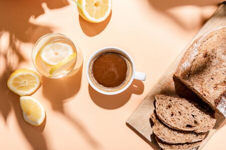 top view of coffee cup, glass of water with lemon and bread for breakfast on beige tableの写真素材