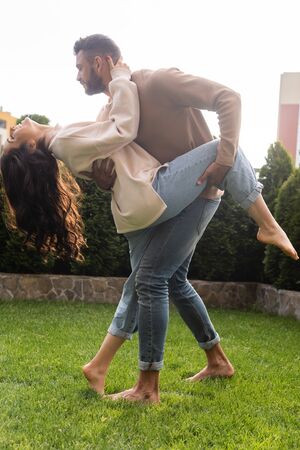 handsome man holding leg of attractive girlfriend while dancing on grass