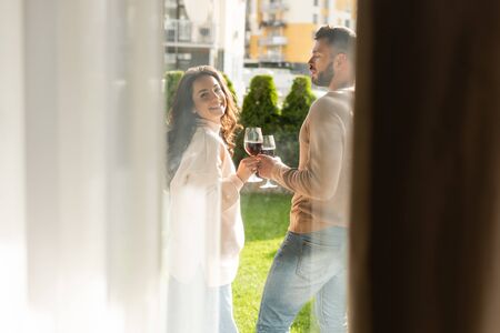 selective focus of man and happy woman standing outside and holding glasses of red wineの写真素材