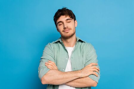 dreamy man with closed eyes standing with crossed arms on blue