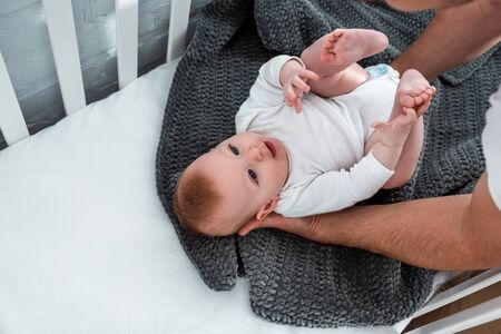 cropped view of man touching cute baby boy lying in baby cot on blanket