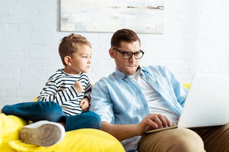 adorable kid looking at attentive father using laptopの写真素材