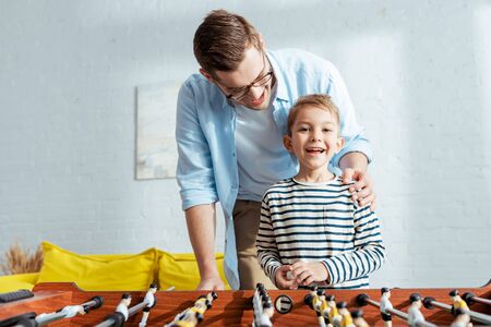 happy boy looking at camera while playing table soccer with fatherの写真素材