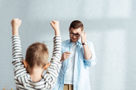 back view of boy showing winner gesture near father touching foreheadの写真素材