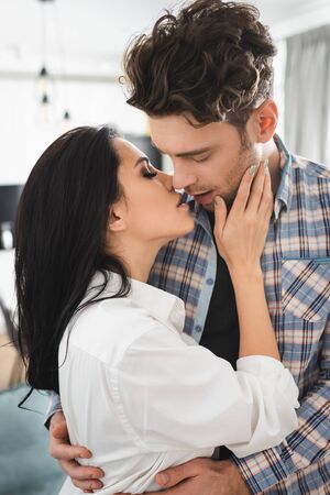 Attractive girl kissing and touching cheek of boyfriend at homeの写真素材