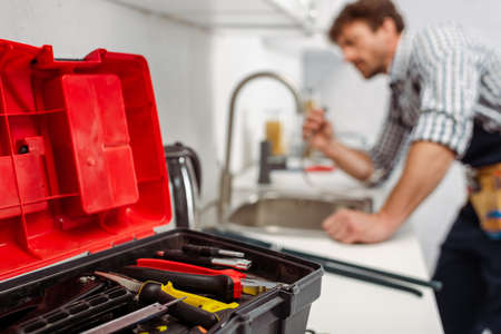 Selective focus of instrument in toolbox and plumber working in kitchen