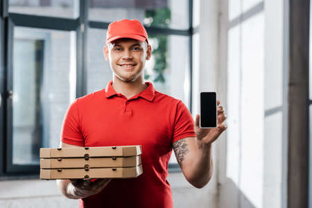 happy delivery man in cap holding smartphone with blank screen and pizza boxesの写真素材