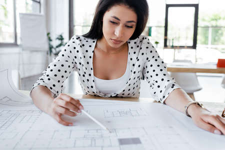 selective focus of pretty businesswoman drawing blueprints in office