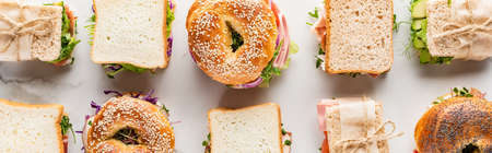 flat lay with fresh sandwiches and bagels on marble white surface, panoramic shot