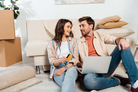 Smiling couple using laptop and credit card on floor during moving