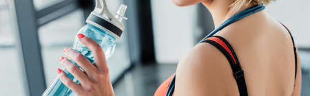 panoramic crop of sportswoman holding sports bottle with water in gym