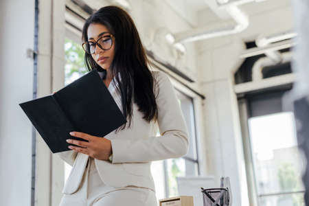 low angle view of attractive businesswoman in glasses looking at notebook in officeの写真素材