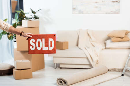 Cropped view of man holding nameplate with sold lettering near cardboard boxes in living room at...