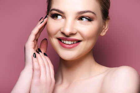 pretty girl with eye shadow and lipstick touching face and smiling on pink