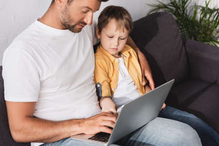 attentive father and son using laptop while sitting on sofa at homeの写真素材