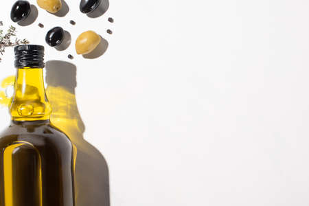 top view of olive oil in bottle near green and black olives and black pepper on white background with shadowの写真素材