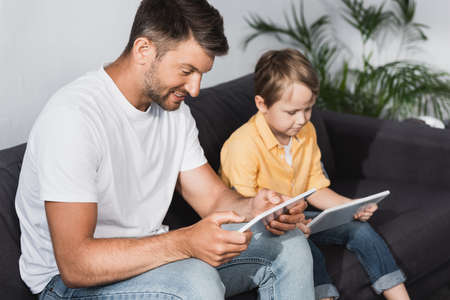 selective focus of smiling father and attentive son using digital tablets at home