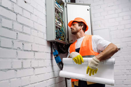 Handsome electrician holding blueprint near electrical distribution boxの写真素材