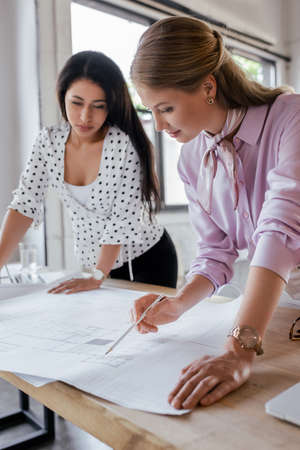 selective focus of attractive businesswomen looking at blueprints in officeの写真素材