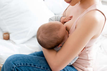cropped view of mother breastfeeding infant son in bedroomの写真素材