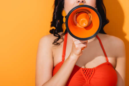 cropped view of young woman screaming in megaphone on orange