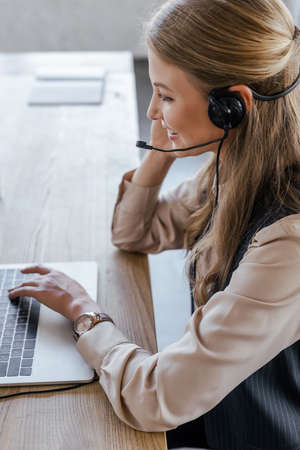 side view of cheerful operator in headset smiling near laptopの写真素材