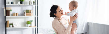 panoramic shot of cheerful mother holding in arms cute infant son in baby romper