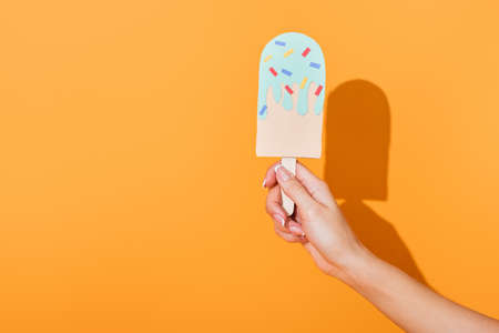 cropped view of young woman holding paper cut ice cream on orangeの写真素材