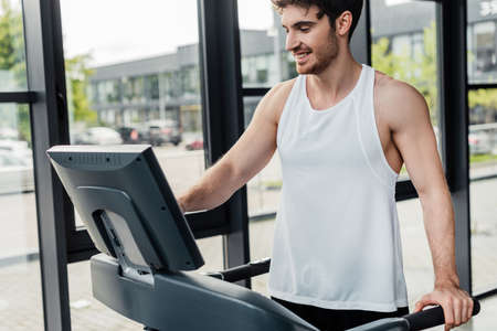 happy sportsman looking at screen on modern treadmill in gymの写真素材