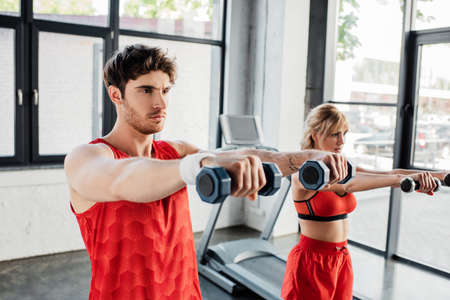 selective focus of man and woman working out with dumbbells in gym