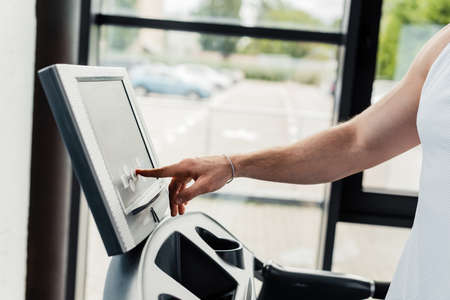 cropped view of sportsman pointing with finger at sensor screen on treadmill in gym