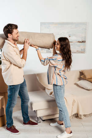 Side view of positive couple holding carpet during relocation in living roomの写真素材
