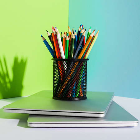 pencil holder with colored pencils on modern laptops on blue, green and white background