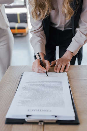 cropped view of businesswoman signing contract near woman in officeの写真素材