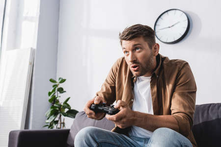 KYIV, UKRAINE - JUNE 9, 2020: excited man playing video game with joystick at home
