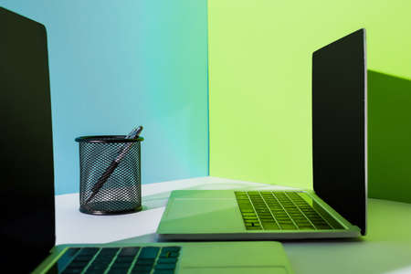 pen in holder near modern laptops on blue, white and green background