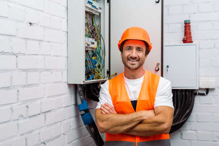 Handsome electrician with crossed arms smiling at camera near electric panelの写真素材