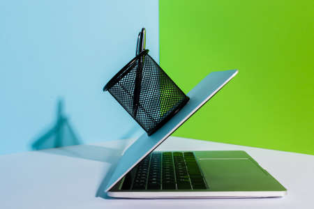 pen in holder on modern laptop on blue, white and green background