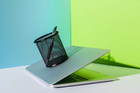 pen in holder on modern laptop on blue, white and green backgroundの写真素材