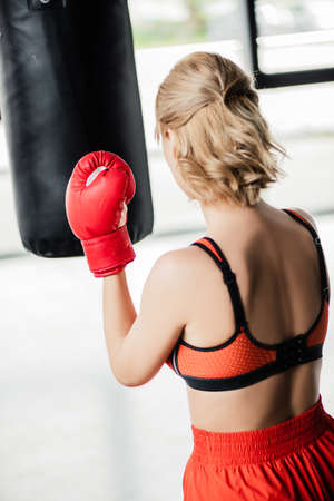 back view of sportive girl in boxing gloves exercising with punching bagの写真素材