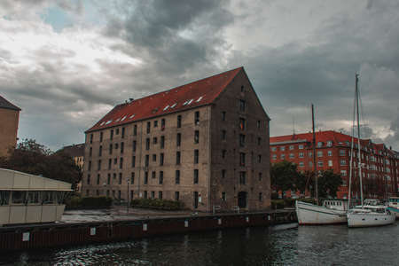 Buildings near harbor and boats on water with cloudy sky at background in Copenhagen, Denmarkの写真素材
