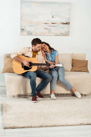 Smiling woman embracing handsome boyfriend playing acoustic guitarの写真素材