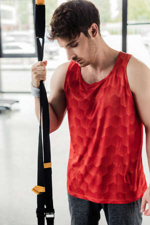 tired sportsman standing and touching resistance bands in gym